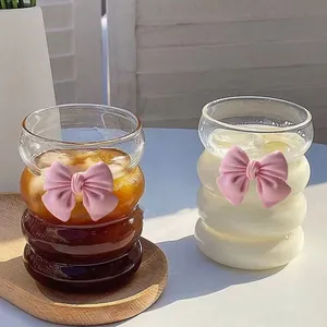 Wavy glass coffee cup with pink bow decoration on a wooden tray with cold drinks