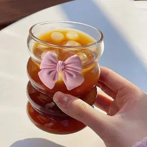 Stylish wavy glass coffee cup with pink bow decoration and straw for cold drinks