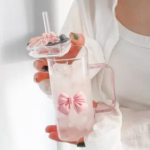 Détail d'un verre transparent avec nœud rose, paille en verre et boisson glacée