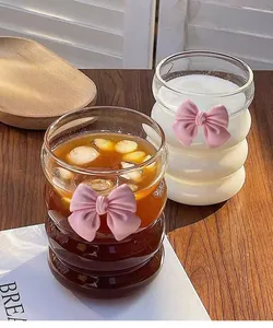 Close-up of wavy glass cup with pink 3D bow decoration on a wooden tabletop