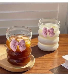 Detail of a wavy glass cup with a 3D pink bow tie accent on a wooden table
