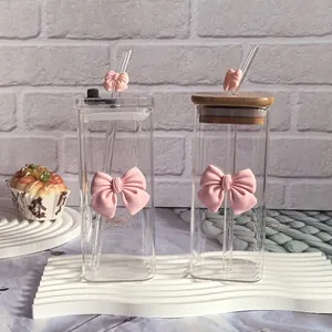 Detail of square glass cups with pink bows, glass straws and bamboo lid on white decor
