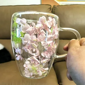Double walled glass coffee mug with pink dried flowers inside and ergonomic handle