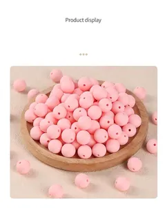 Detail shot of light pink matte 12mm silicone beads with thread holes on wood tray