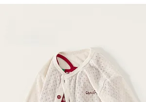 Detailed view of cream baby cardigan featuring hollow diamond knit and red button accents