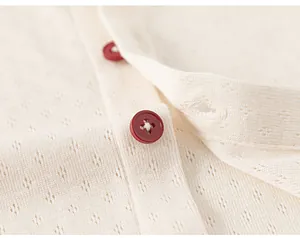 Detailed macro view of pointelle knit fabric with red round buttons on cream white top