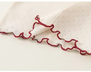 Close-up of knit fabric with diamond cutouts and scalloped red embroidered edges