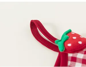 Detailed macro shot of red knit straps with 3D strawberry patches and gingham fabric