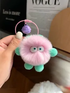 Close-up of a pink plush pompom keychain with green limbs and a purple bell accessory