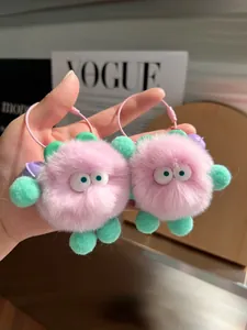 Detailed view of pink plush charms with big eyes and mint green pom-pom legs