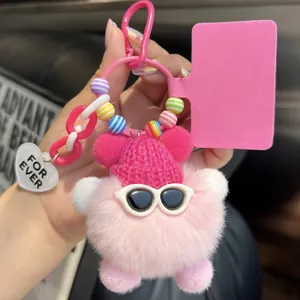 Close-up of pink plush pompom keychain with sunglasses and a red knitted hat