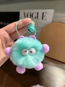 Close-up of mint green plush monster keychain with purple ears and a bell detail