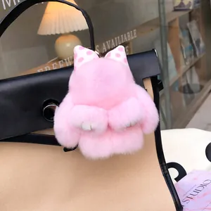 Pink rabbit fur bag charm with polka dot bow displayed on a canvas shoulder bag