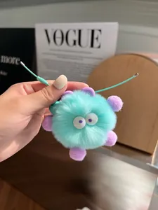 Detail of a mint green fluffy plush keychain with purple accents held in a hand