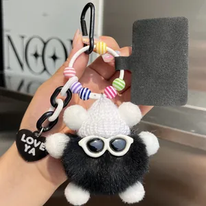 Close-up of fluffy black teddy bear charm with white hat, sunglasses and heart tag