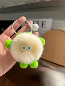 Detail of a fluffy cream monster keychain with green ears, big eyes and a white bell