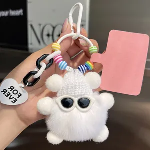 Close-up of white plush bear pendant with sunglasses, knit hat, and heart charm