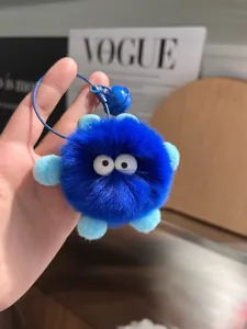 Close-up of fluffy blue monster keychain with big white eyes and small bell on a hand