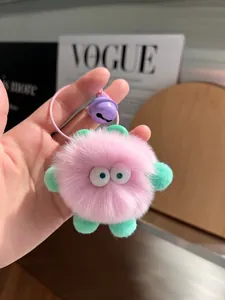 Detail of pink faux fur pompom keychain with green ears and a purple metallic bell