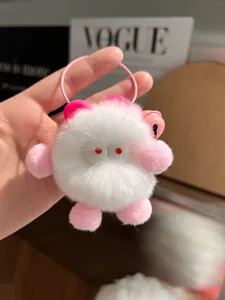 Close-up of cute plush monster keychain with soft white fur and pink woven lanyard charm