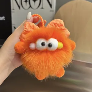 Detalle del llavero de monstruo de peluche naranja con ojos grandes y un lazo suave