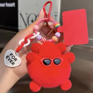 Close-up of a fluffy red plush monster keychain with sunglasses and colorful beads