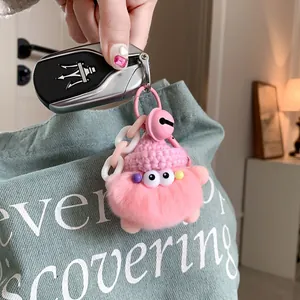 Detail of a pink plush monster keychain with fluffy faux fur and a knit hat on a blue bag