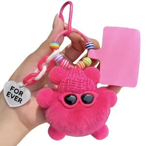 Pink plush bear keychain with sunglasses and knitted hat on a white background