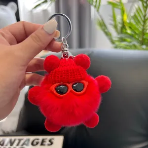 Detail of red plush keychain with knitted hat and sunglasses held in hand