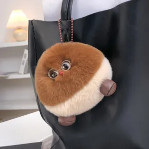 Llavero de peluche marrón y beige con forma de castaña en bolso de cuero negro