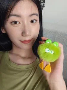 Detailed shot of a green plush frog keychain charm held by a woman in a green shirt