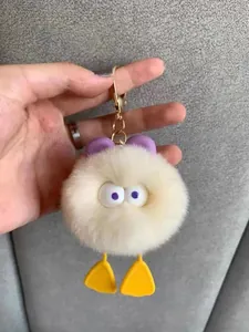 Close-up of white plush duck keychain with purple bow and golden metal lobster clasp