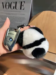 Close-up of fluffy panda faux fur pompom keychain attached to a car key on a magazine