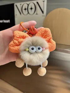 Close-up of beige plush pompom keychain with orange bow and matching bell accessory