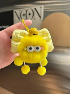 Detail of a yellow plush monster keychain with a checkered bow and bell on a bag