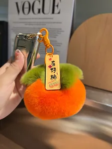 Dettaglio portachiavi a forma di cachi in peluche arancione con etichetta Good Luck e foglia