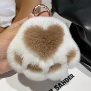 Close-up of fluffy white cat paw plush keychain with brown heart patterns and gold ring