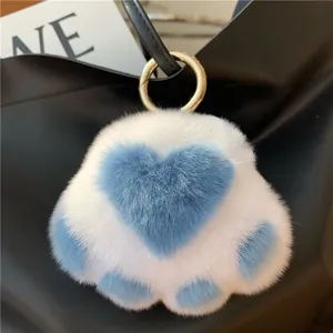 Close-up of a soft blue and white cat paw plush keychain on a black leather handbag
