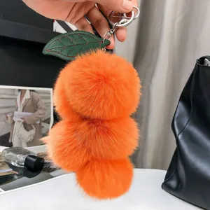 Dettaglio portachiavi a uva in finta pelliccia arancione con foglie su borsa in pelle