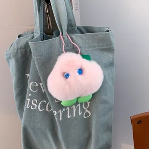 Cute pink peach plush keychain accessory on denim bag with soft fuzzy texture