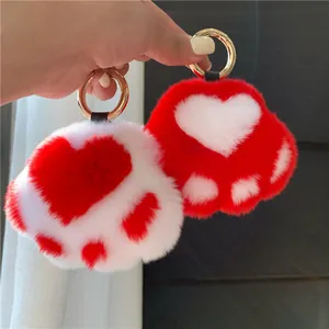 Detail of red and white cat paw plush keychains with golden rings held in hand
