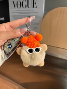 Détail du porte-clés en peluche avec bonnet orange et lunettes de soleil tenu près d'une clé