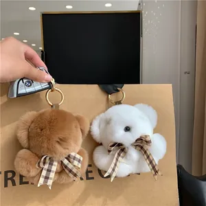 Detail of plush brown and white rabbit fur bear keychains with checkered bows on a paper bag