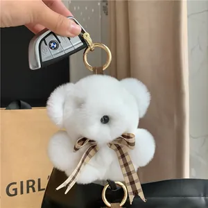 Close-up of white plush bear pendant with brown plaid bow and gold metal keychain