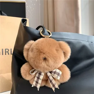 Close-up of brown plush bear charm with plaid bow and gold clasp on a leather bag