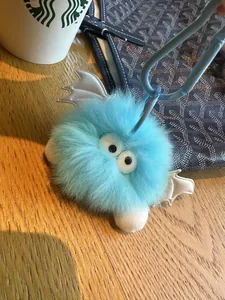 Close-up van lichtblauwe pluche monster sleutelhanger met witte leren vleugels op houten tafel