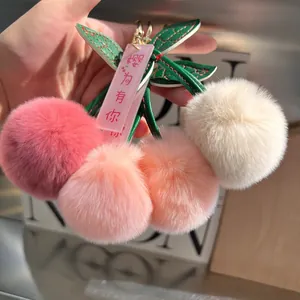 Plush cherry keychain with soft fur balls in pink tones and green leather leaf detail