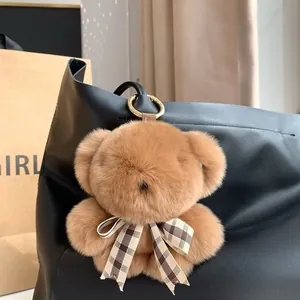 Cute brown plush teddy bear keychain with plaid bow on a black leather bag