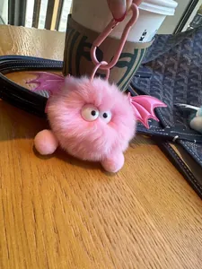 Detail van roze harige monster sleutelhanger met vleugels naast een kopje koffie