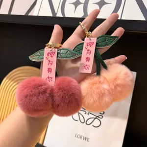 Close-up of fluffy faux fur cherry bag charms in red and pink with leather leaf detail